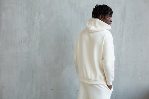 Stylish man in white hoodie standing near wall
