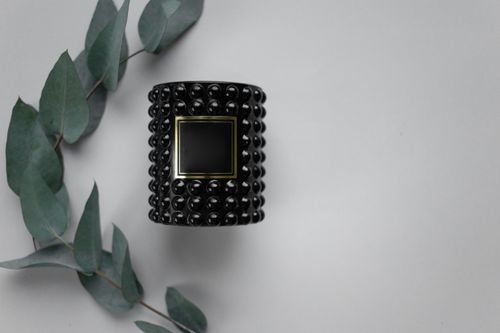 Free Sophisticated black candle holder with textured design, paired with green eucalyptus leaves on a gray background. Stock Photo
