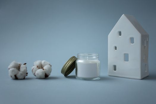 A serene arrangement of a candle, cotton bolls, and a ceramic house on a gray background.