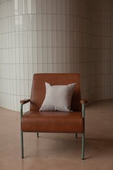 Stylish tan leather chair with white pillow in a minimalist, modern interior with tiled walls.