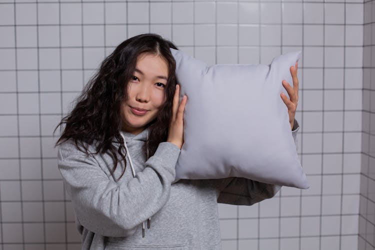 A Woman In Gray Hoodie Holding A Pillow