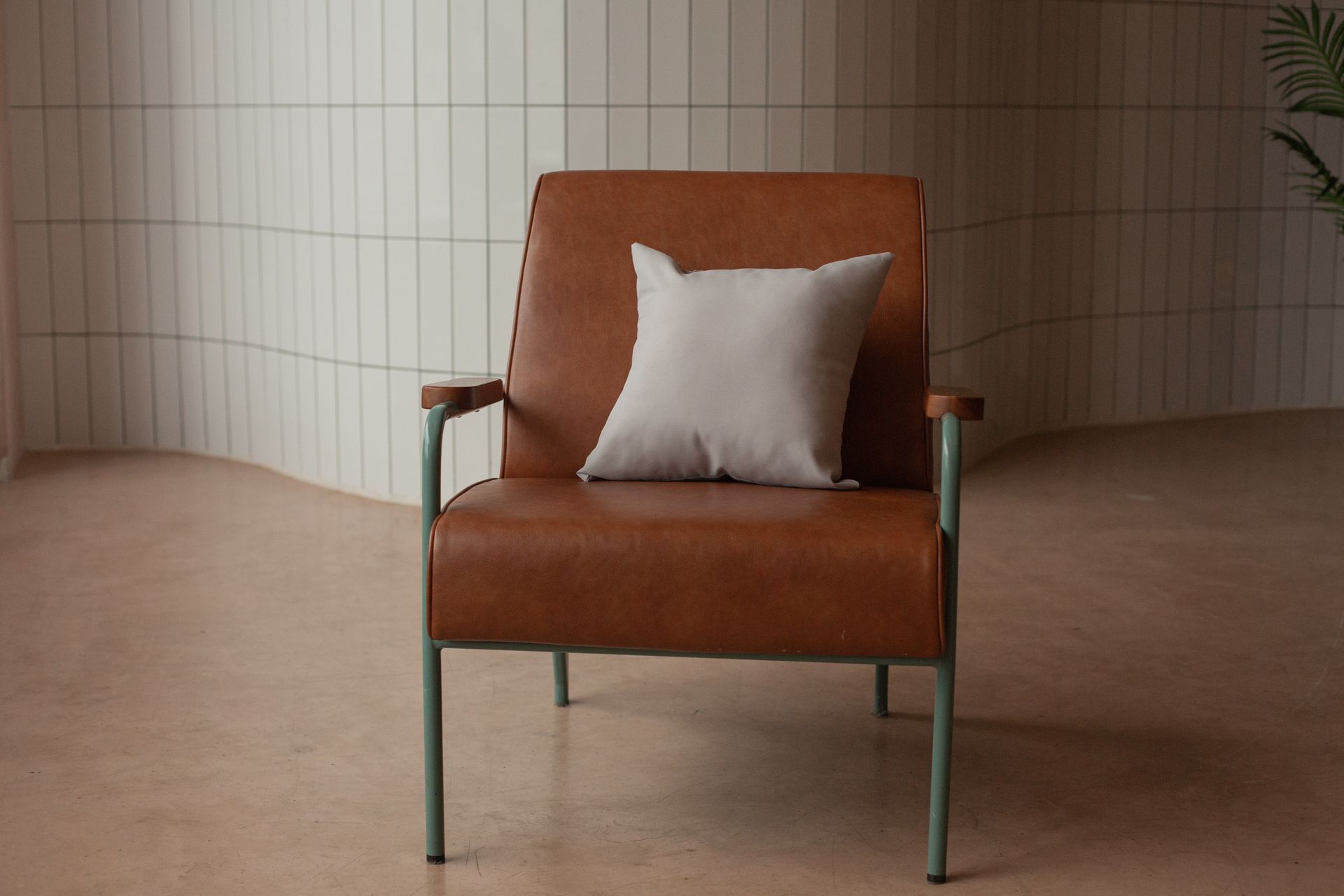 A brown leather chair with a white pillow in a minimalist indoor setting.