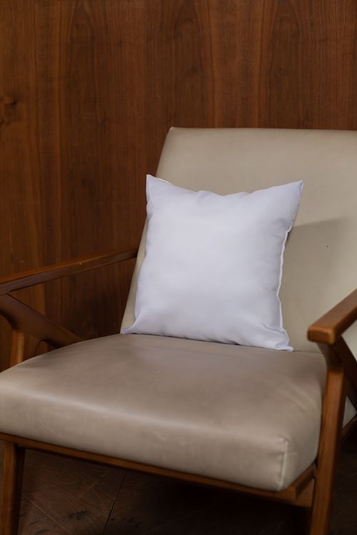 Free Elegant beige chair with white pillow set against a warm wooden backdrop, embodying comfort and style. Stock Photo