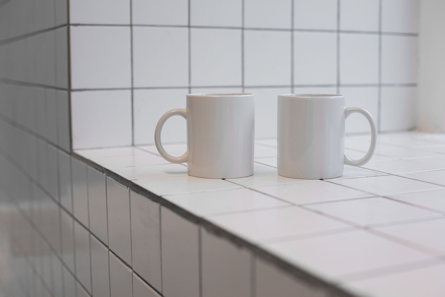 Two white ceramic mugs placed on a clean tiled surface, perfect for minimalistic and modern design themes.