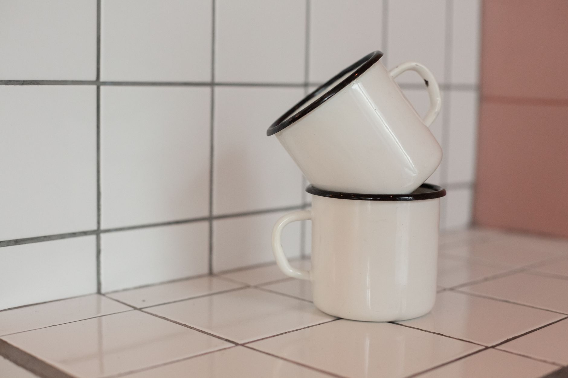 Two white enamel mugs stacked on a tiled kitchen counter, creating a vintage look.