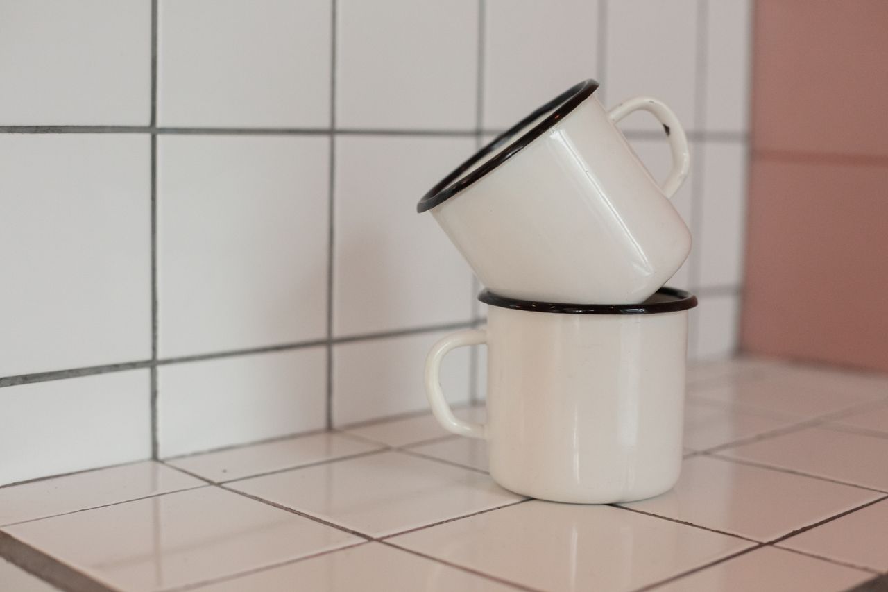 two white enamel mugs stacked on a tiled kitchen counter creating a vi