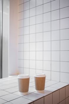 Two paper coffee cups on a white tiled surface with copy space, perfect for café ambiance.