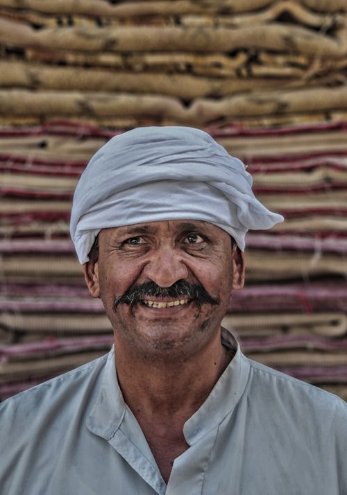 Free Portrait of a smiling Middle Eastern man wearing a traditional turban with textiles in the background. Stock Photo