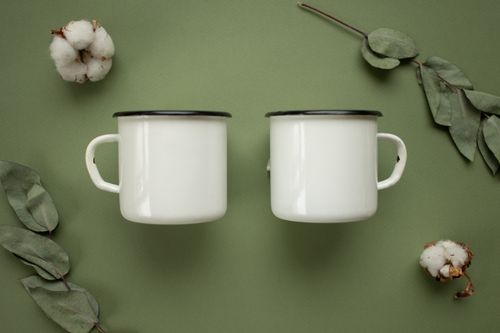 Free Top view of two white mugs with eucalyptus leaves and cotton on a green background. Stock Photo