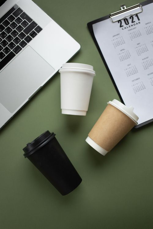 Free Minimalist flat lay of coffee cups, laptop, and 2021 calendar on green background. Stock Photo