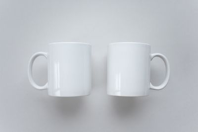 A pair of plain white ceramic mugs on a pale surface, photo by KATRIN BOLOVTSOVA on Pexels