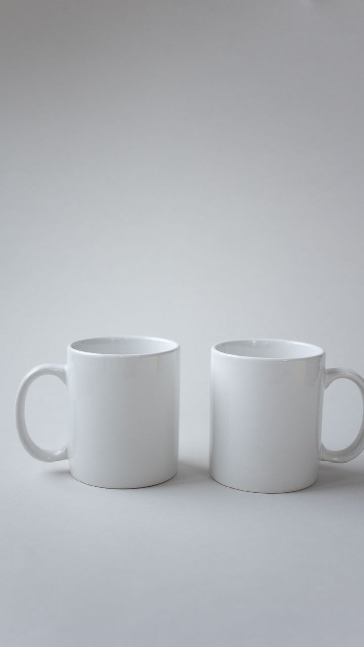 set of matching white ceramic coffee mugs stacked on a wooden shelf