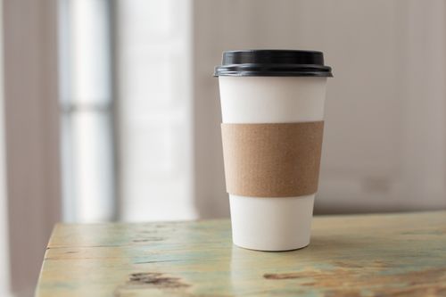 Free White paper coffee cup with brown cardboard sleeve on a rustic table indoors. Stock Photo