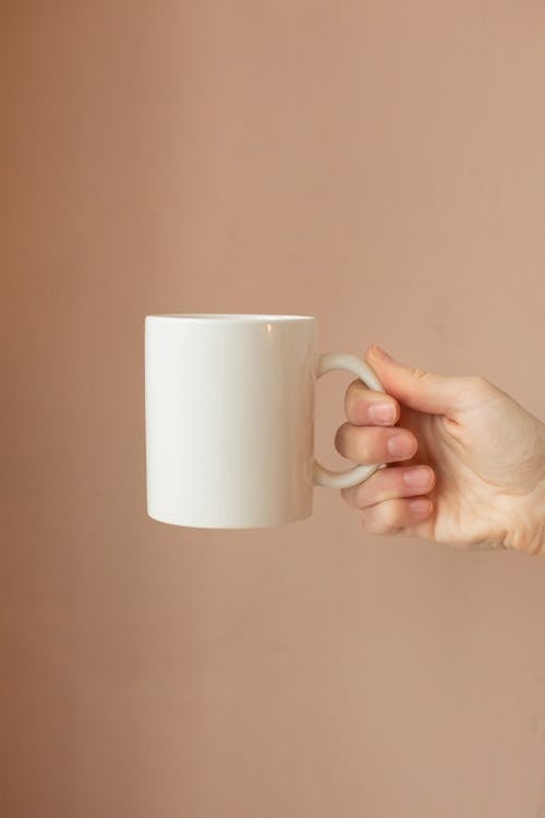 Free A Hand Holding a White Ceramic Mug Stock Photo