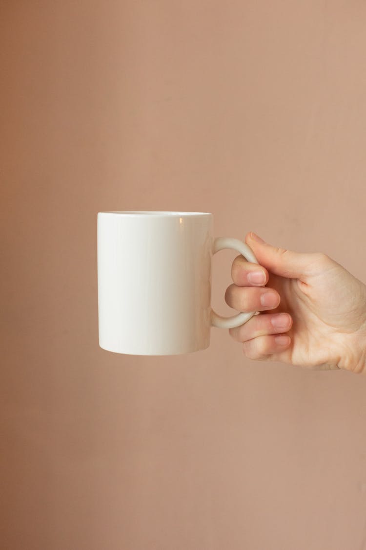 A Hand Holding A White Ceramic Mug