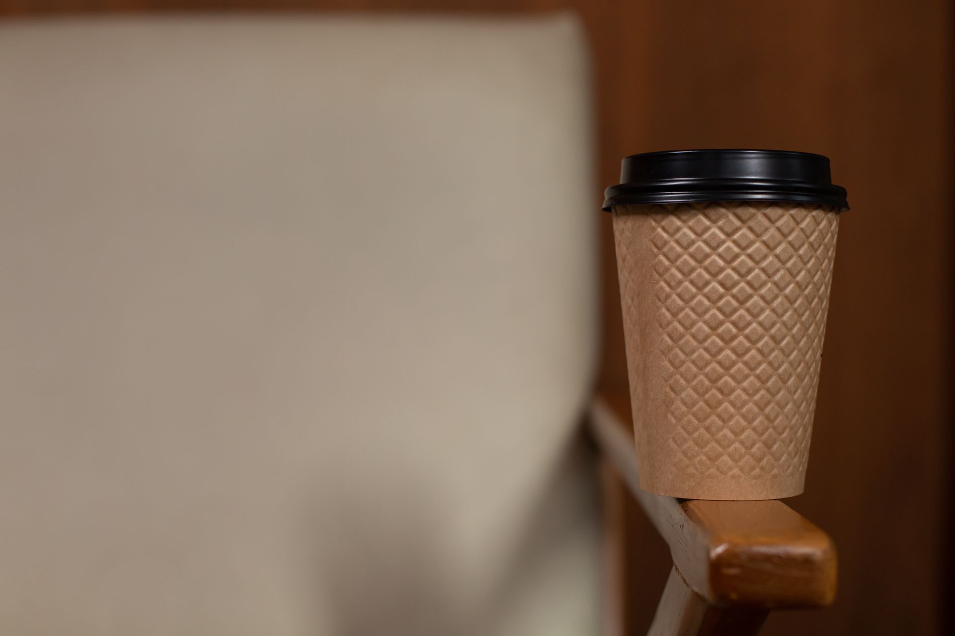 Close-up of a textured disposable coffee cup on a wooden chair armrest, ideal for beverage and lifestyle themes.