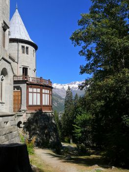 Castel Savoia in Italy amidst lush trees and a mountain backdrop under a blue sky.