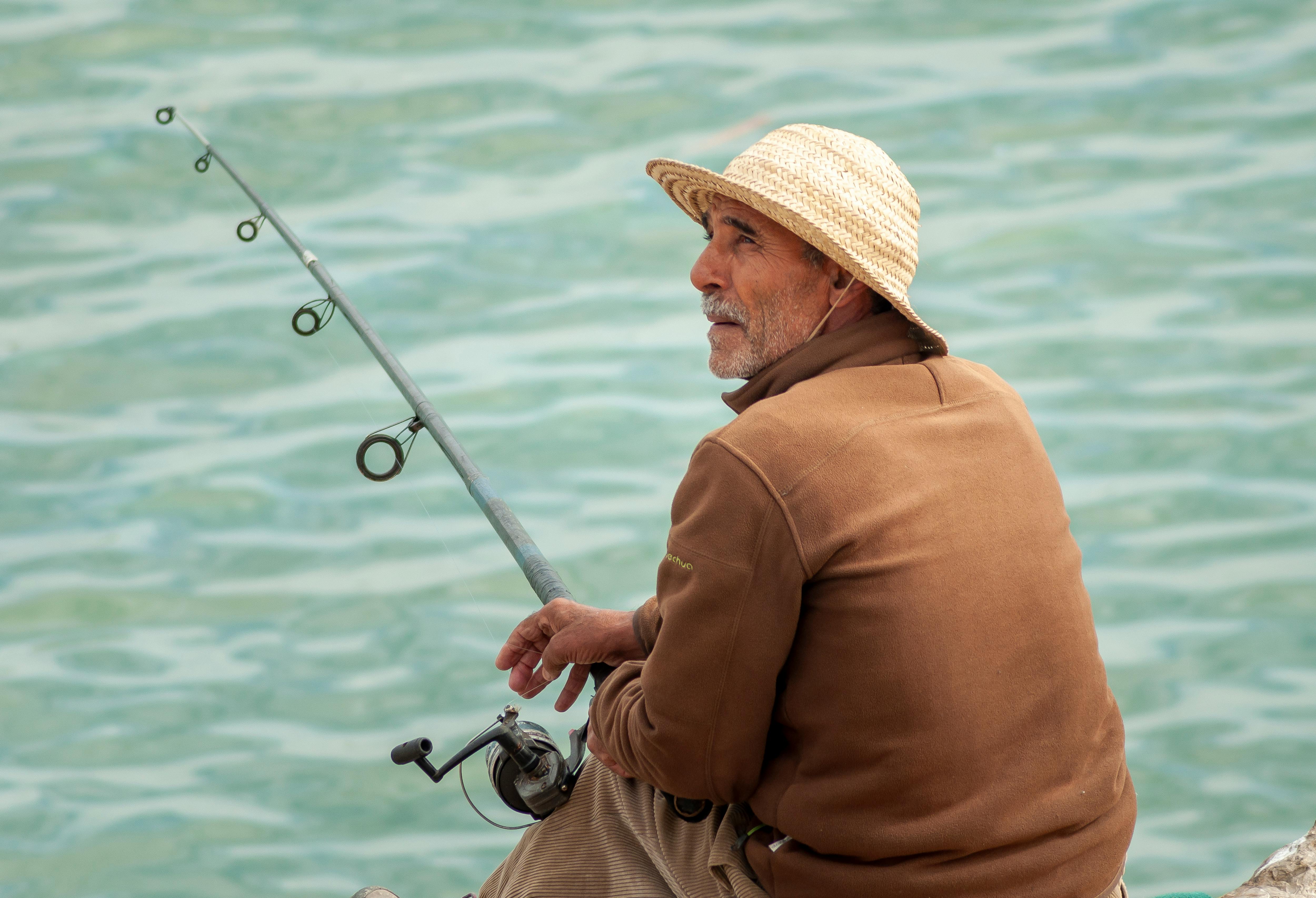 Pensive elderly ethnic man catching fish with rod and sitting on seashore ·  Free Stock Photo