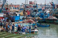 Group of unrecognizable fishermen in casual clothes standing on wooden pier near various old boats before catching fish in sea on cloudy day
