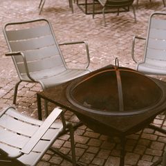 A square fire pit with a mesh lid among garden chairs
