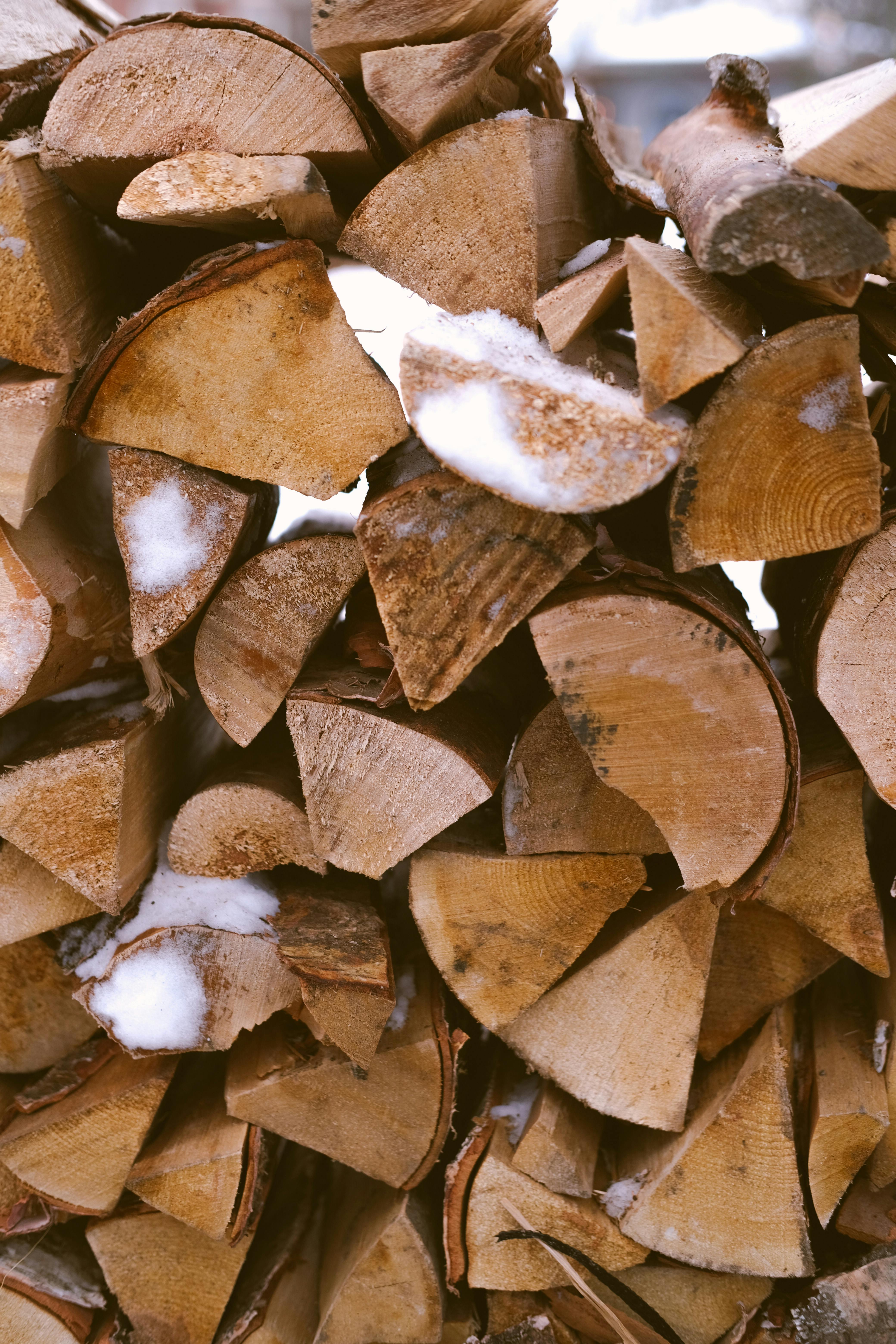 Close-up of stacked wood logs with snow, ideal for winter themes and organic textures.