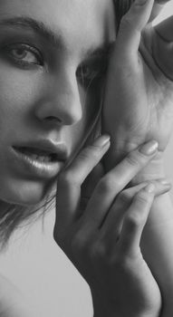 Monochrome close-up portrait of a woman with expressive eyes and delicate hands.