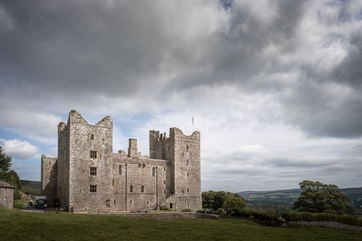 Medieval Bolton Castle in England with a dramatic cloudy skyline, showcasing its historical architecture.