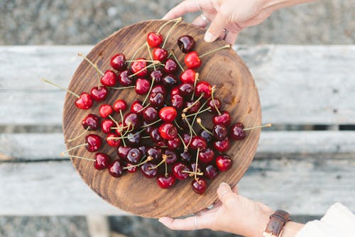A Person Holding Wooden Plate with Fresh Cherries
