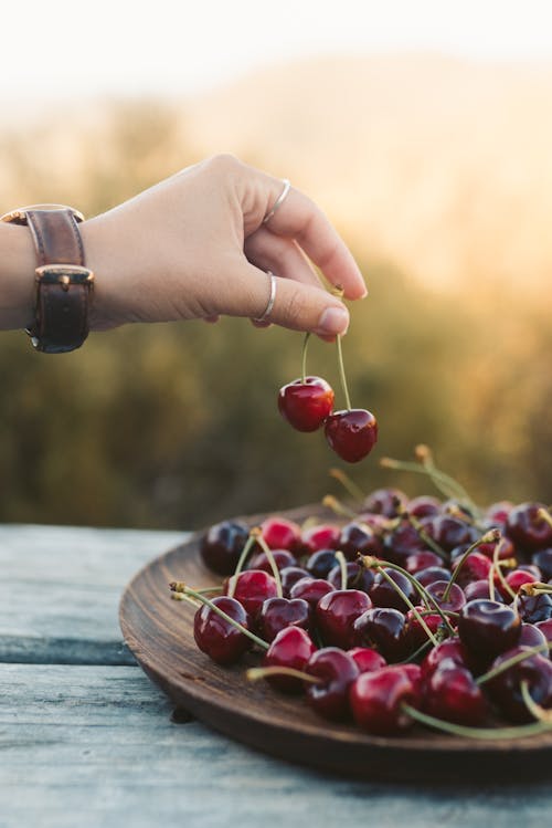 A Hand Getting Red Cherries From the Wooden Plate