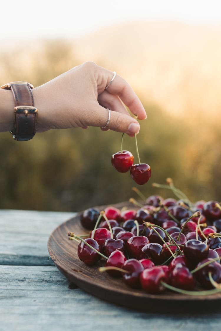 A Hand Getting Red Cherries From The Wooden Plate