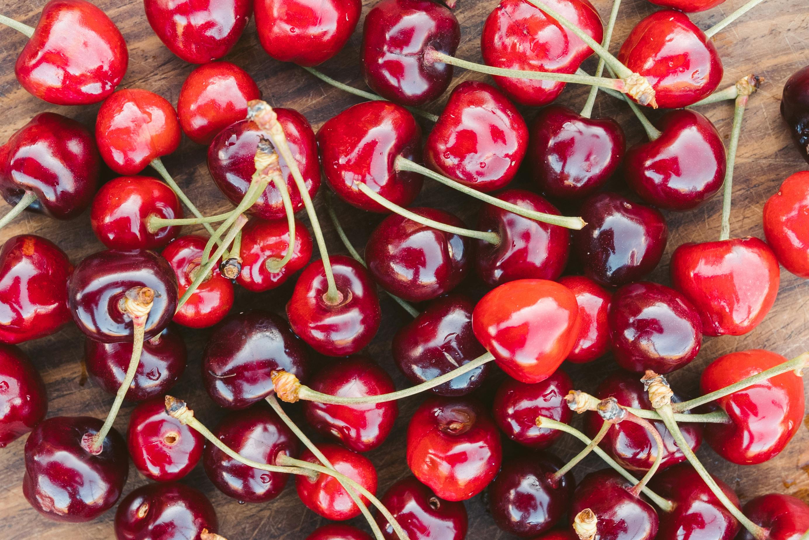 A close-up photo of vibrant fresh cherries scattered on a wooden table.Cherries and Heart Health.