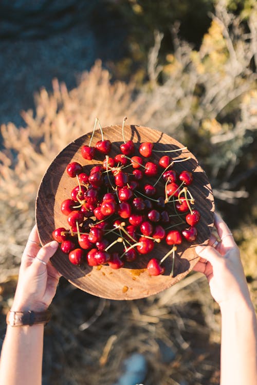 A Person Holding a Wooden Plate with Red Cherries