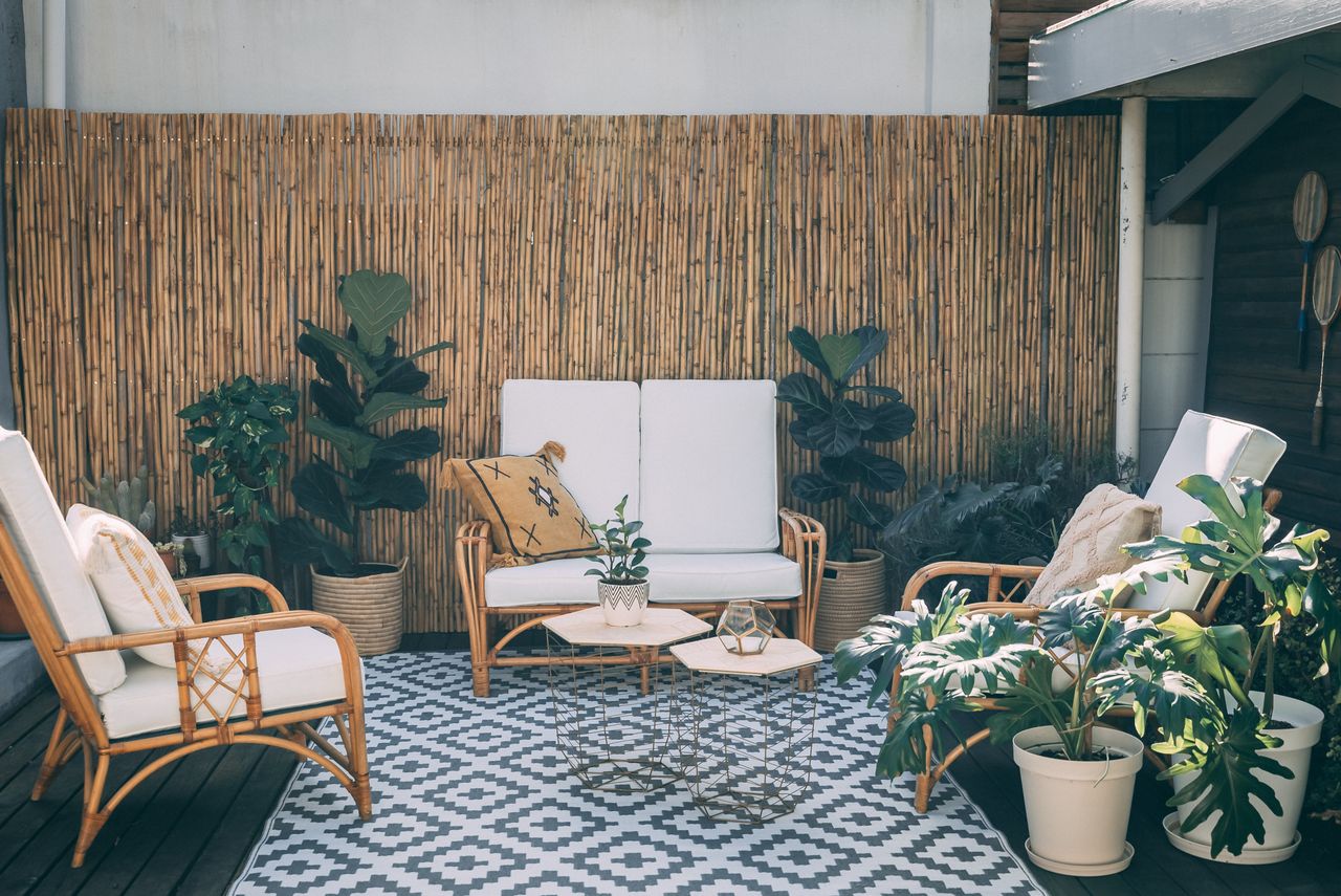 Patio seating area softened by large potted plants and a tall bamboo privacy screen, with rattan chairs, an outdoor rug and small tables