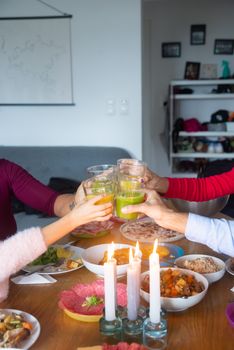 Friends sharing a joyful toast with drinks around a cozy dinner table lit by candlelight.