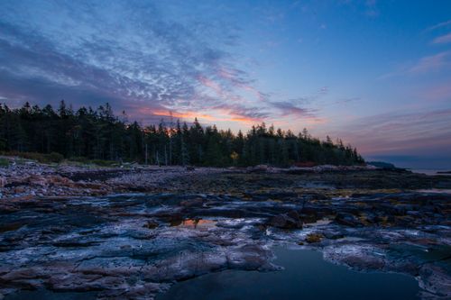 Free Tranquil twilight view featuring rocky shoreline and lush forest with a beautiful sky reflection. Stock Photo