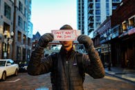 A Person in a Puffer Jacket a Holding a Placard in the Street