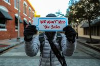 A Person in a Puffer Jacket a Holding a Placard in the Street