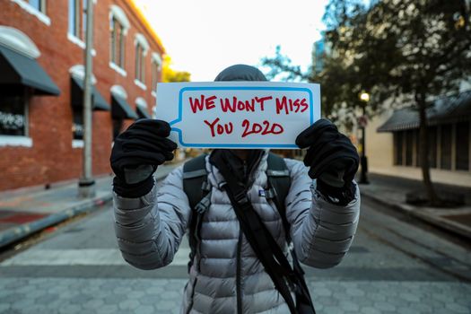 An individual in warm clothing holds a 'We Won't Miss You 2020' sign on a street in Orlando, Florida.