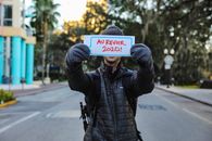 A Person in a Puffer Jacket a Holding a Placard in the Street