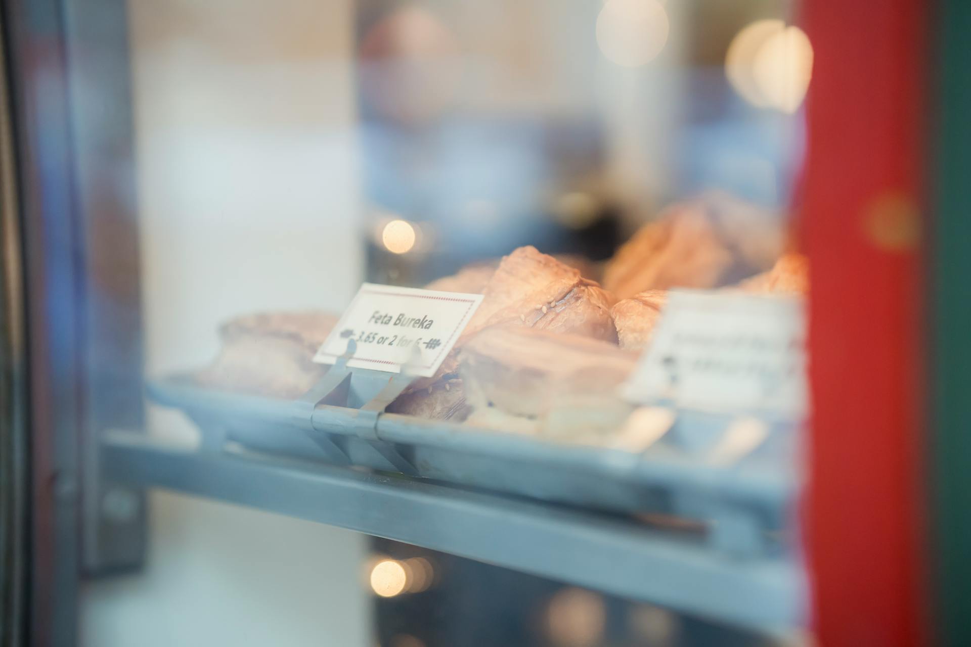 Through glass of assorted delicious desserts with prices placed on metal display of bakery shop on street on blurred background