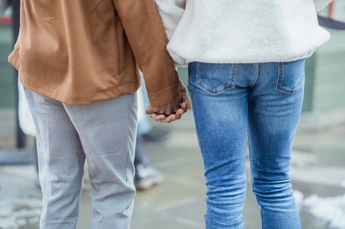 Free Back view of unrecognizable romantic couple wearing casual clothes holding hands while standing on sidewalk with snow in city on blurred background Stock Photo