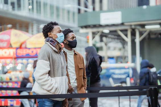Side view of serious African American homosexual couple wearing protective masks standing on street in city on blurred background during pandemic