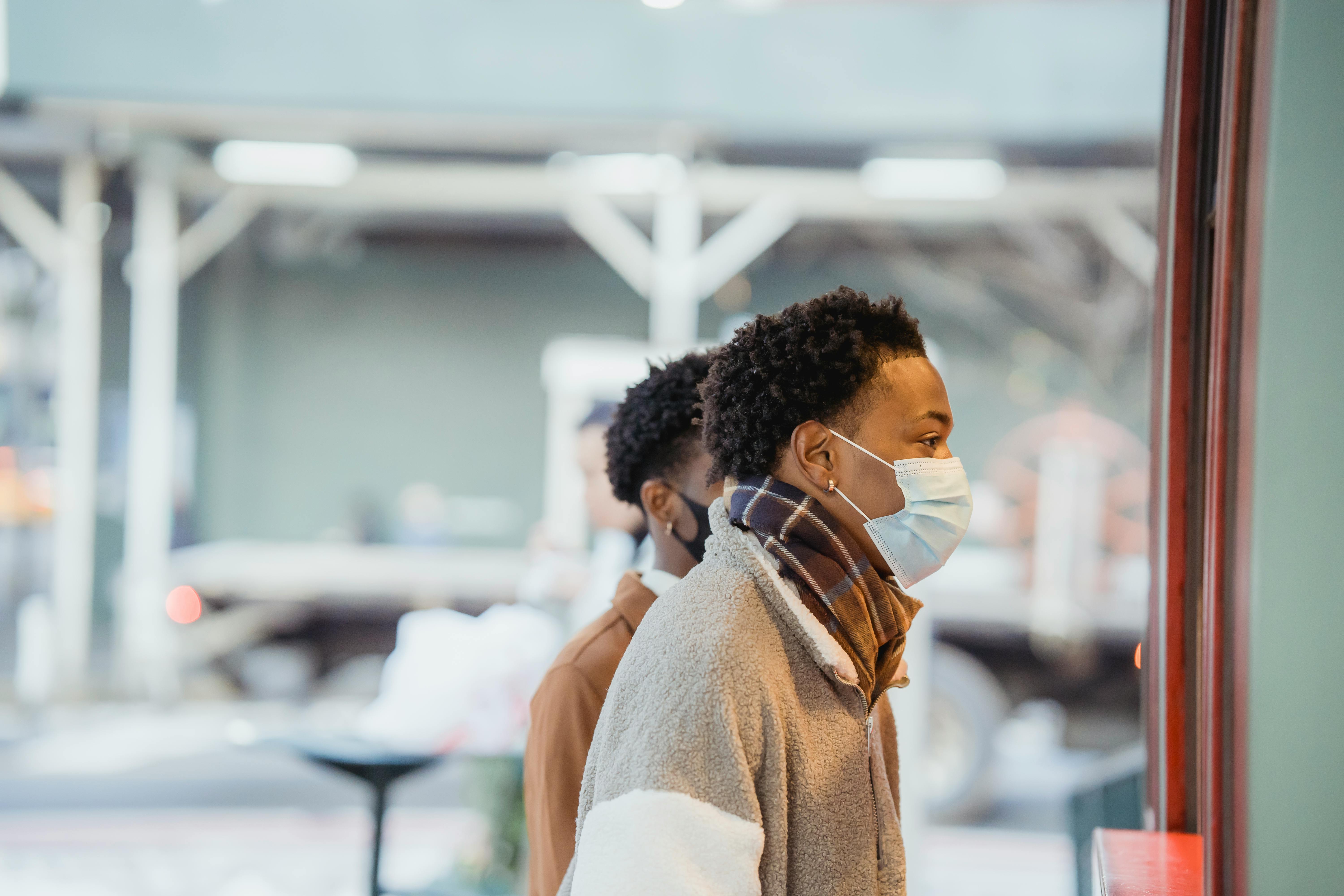 black men in medical masks standing near building on street