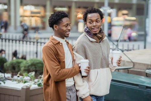 Free Positive African American homosexual male couple with takeaway coffee strolling on street with buildings on blurred background during date in city Stock Photo