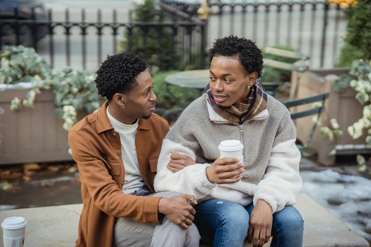 Cheerful Black Gays With Coffee Sitting On Bench