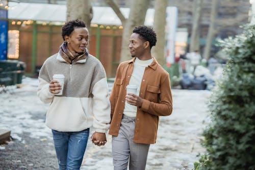 Black homosexual couple walking on street with coffee