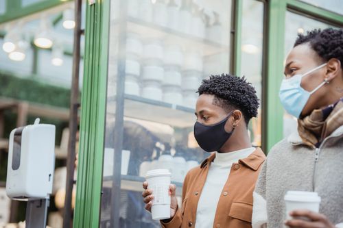 Free African American male couple with tasty takeaway hot beverages strolling on street near building while spending time together in city Stock Photo