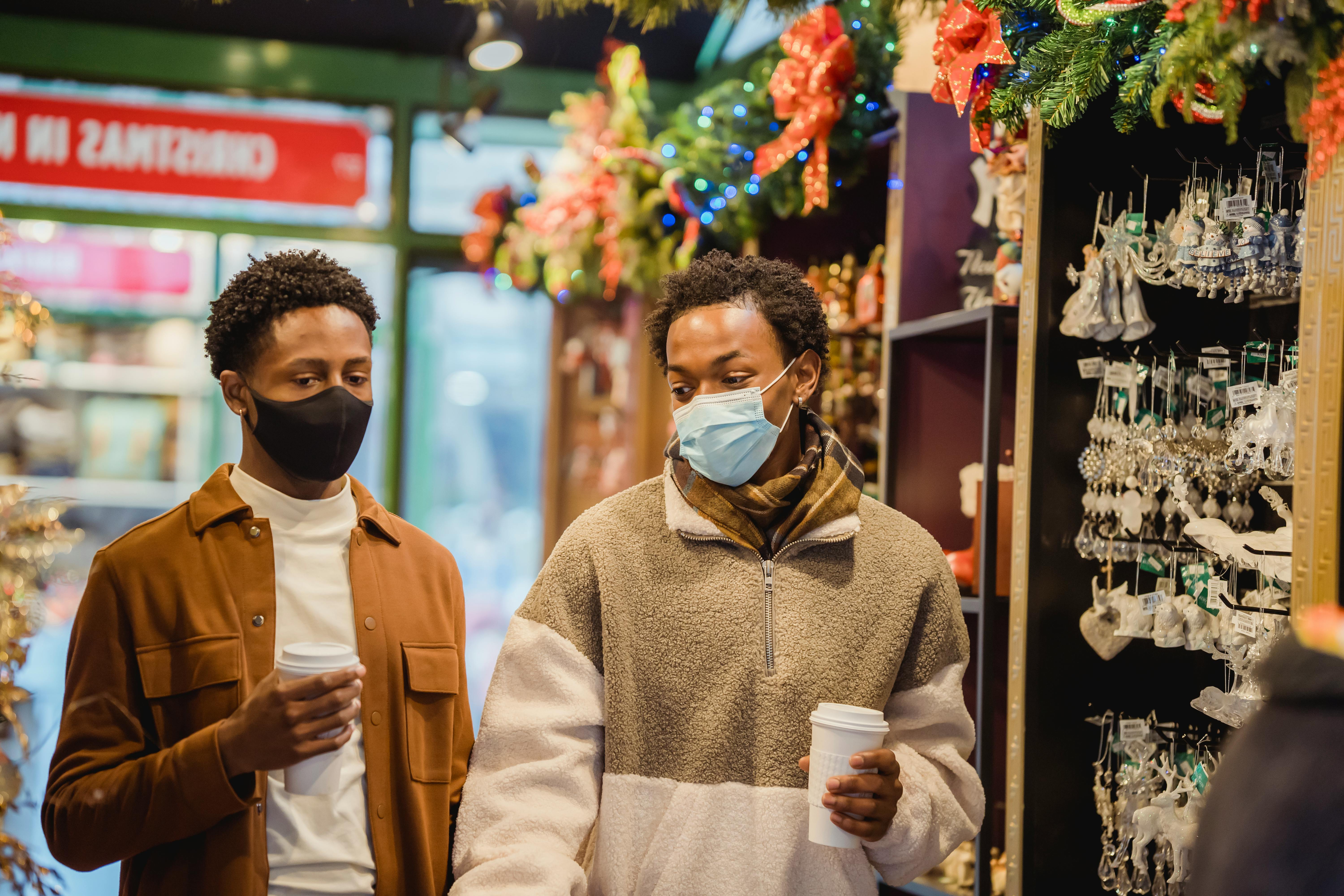 Two men wearing masks shop for Christmas decorations in a festive store.