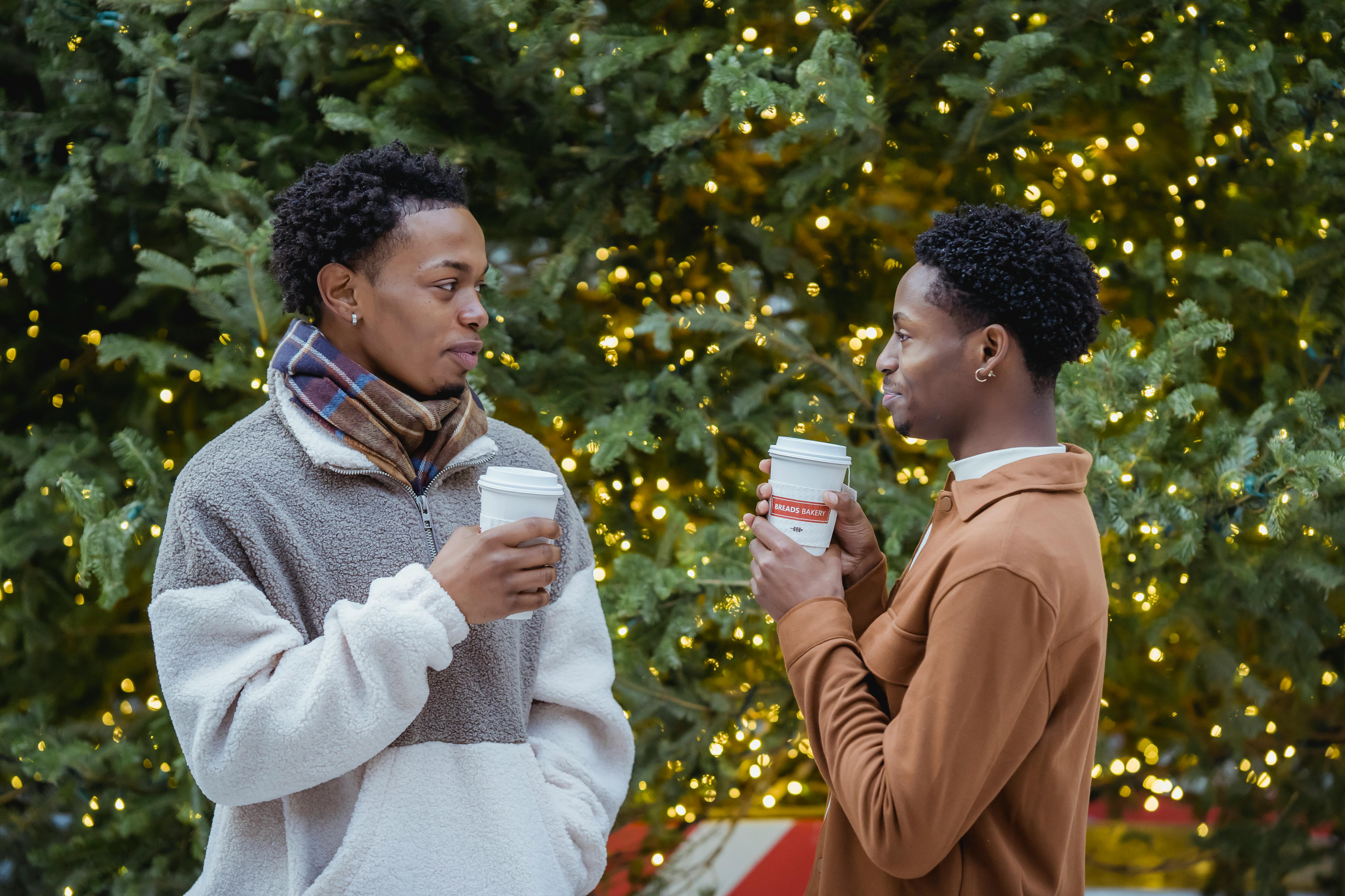happy black gays drinking takeaway coffee near christmas tree on street