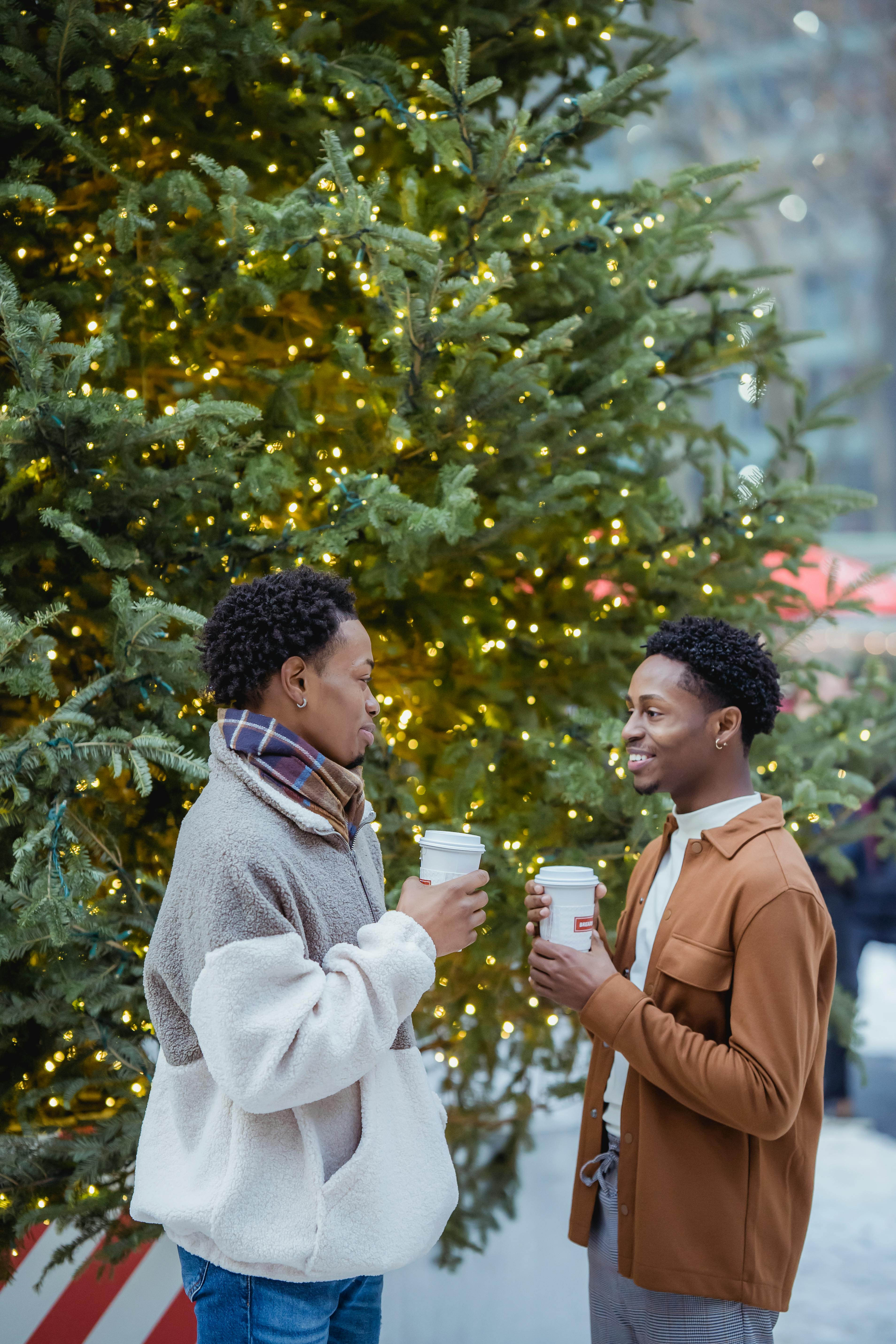 happy young african american guys drinking takeaway coffee on street near christmas tree